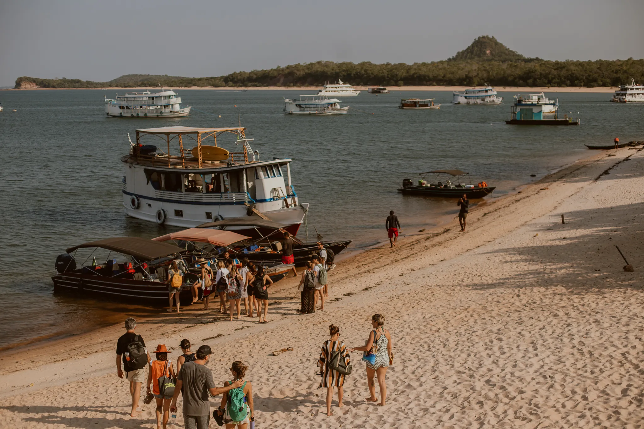 A group of guests with backpacks walking across the sand toward the anchored boats