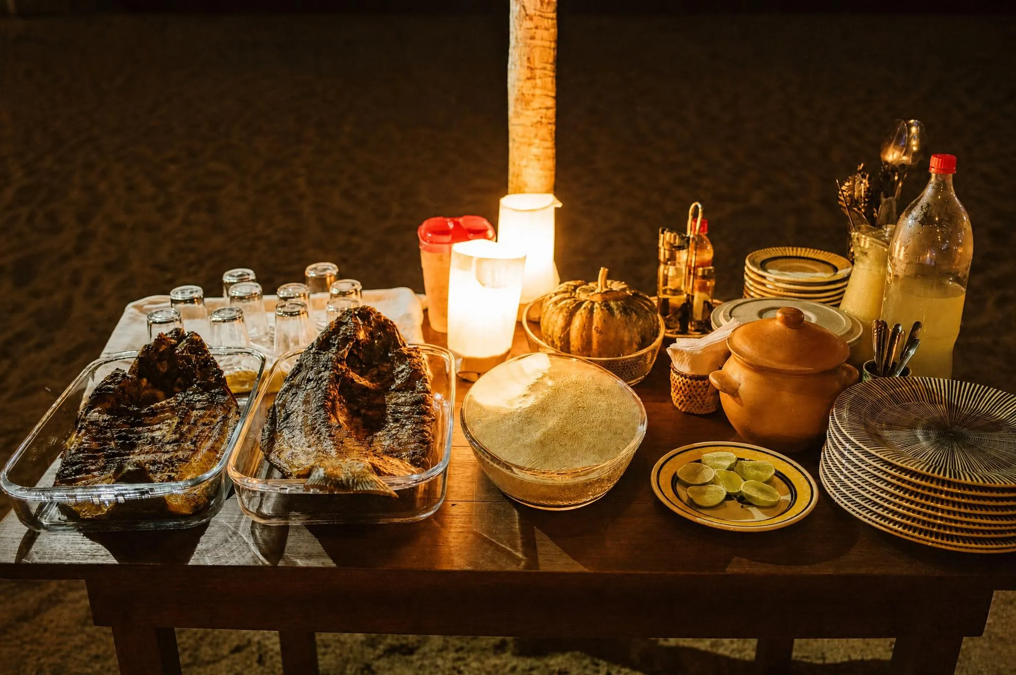 Peixes assados inteiros em travessas de barro à luz de velas, com farofa e limão ao lado